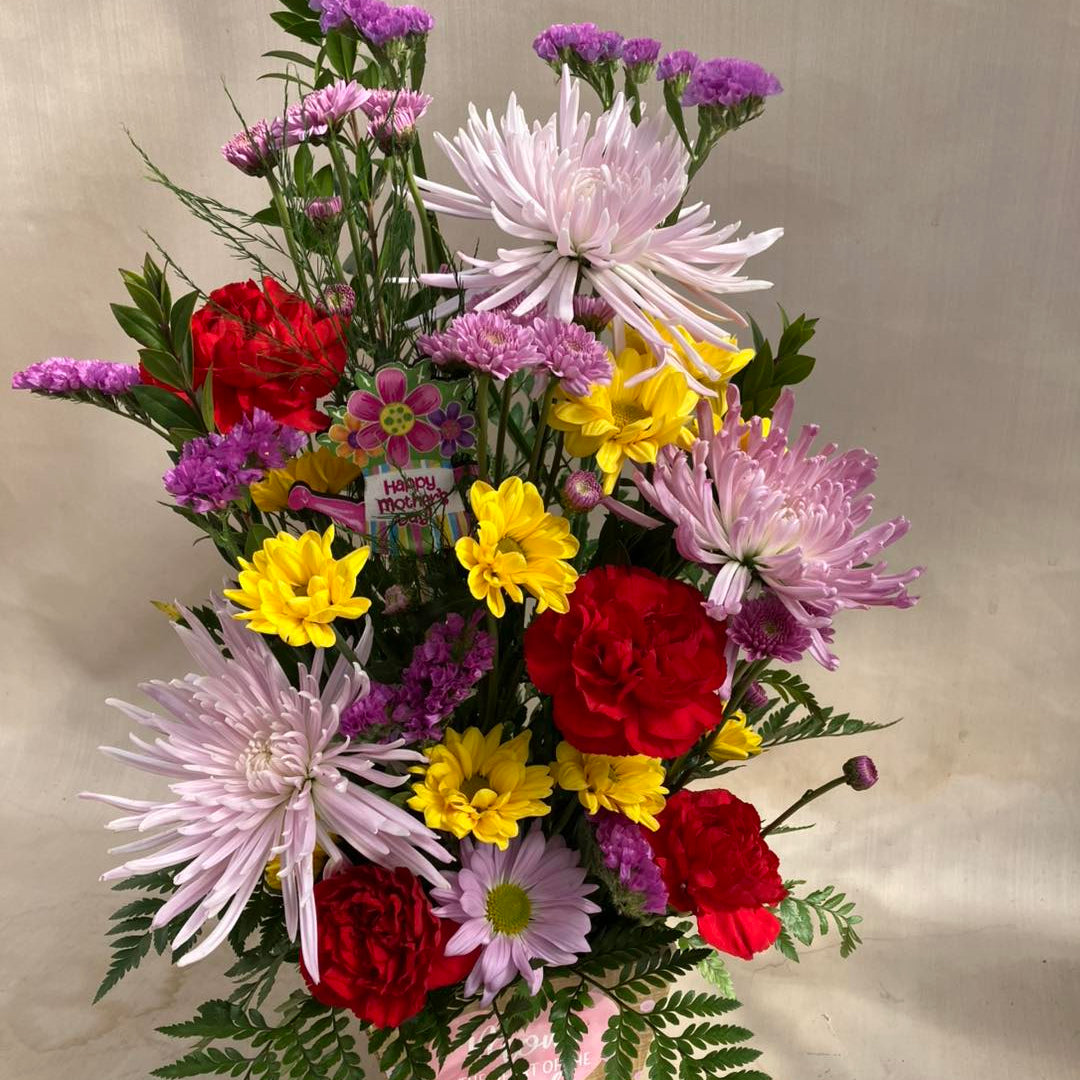 Bouquet of colorful flowers including red, yellow, and pink flowers in a box on a beige background