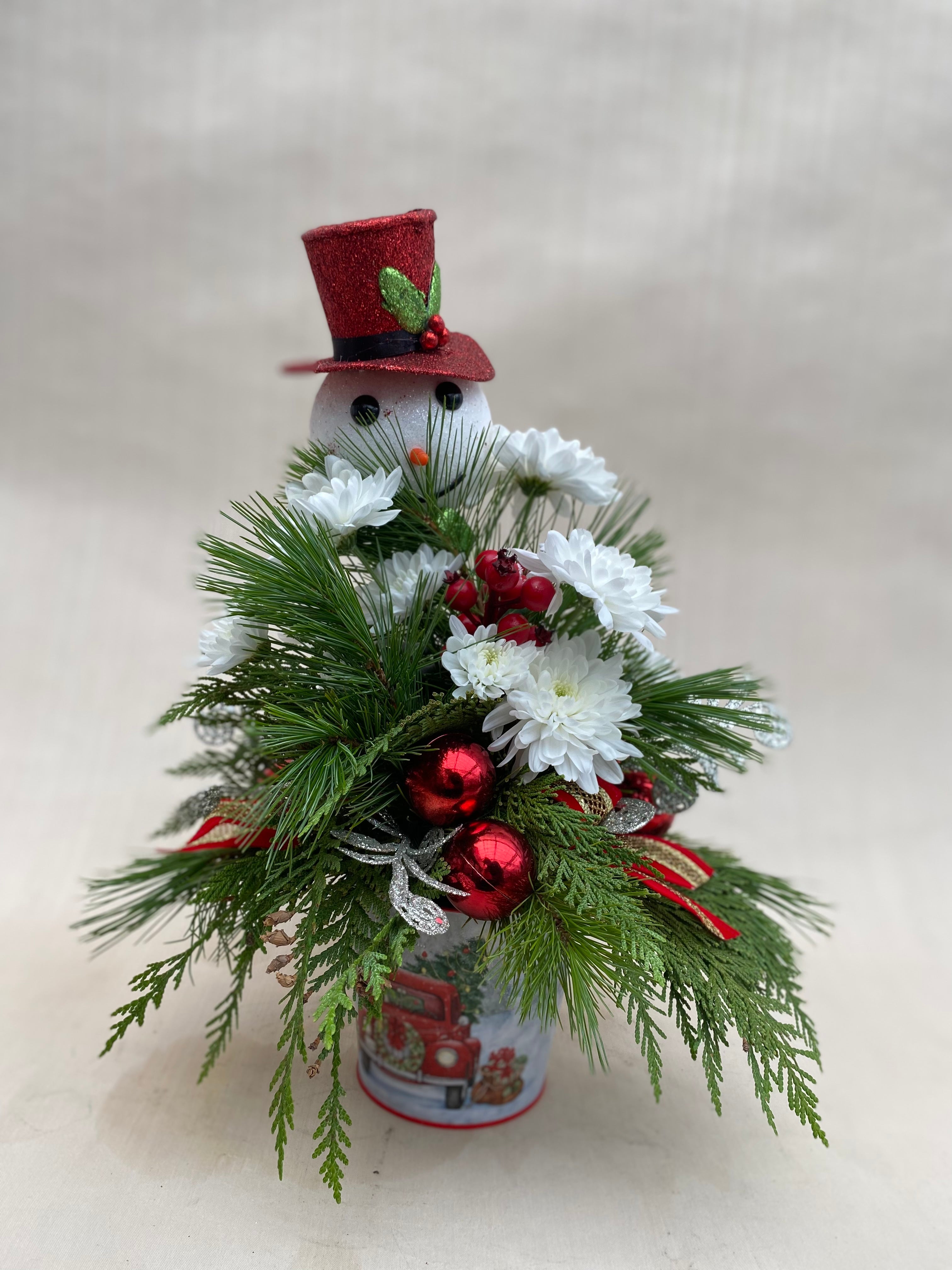 Decorative snowman topiary with greenery, white flowers, and red accents on a neutral background